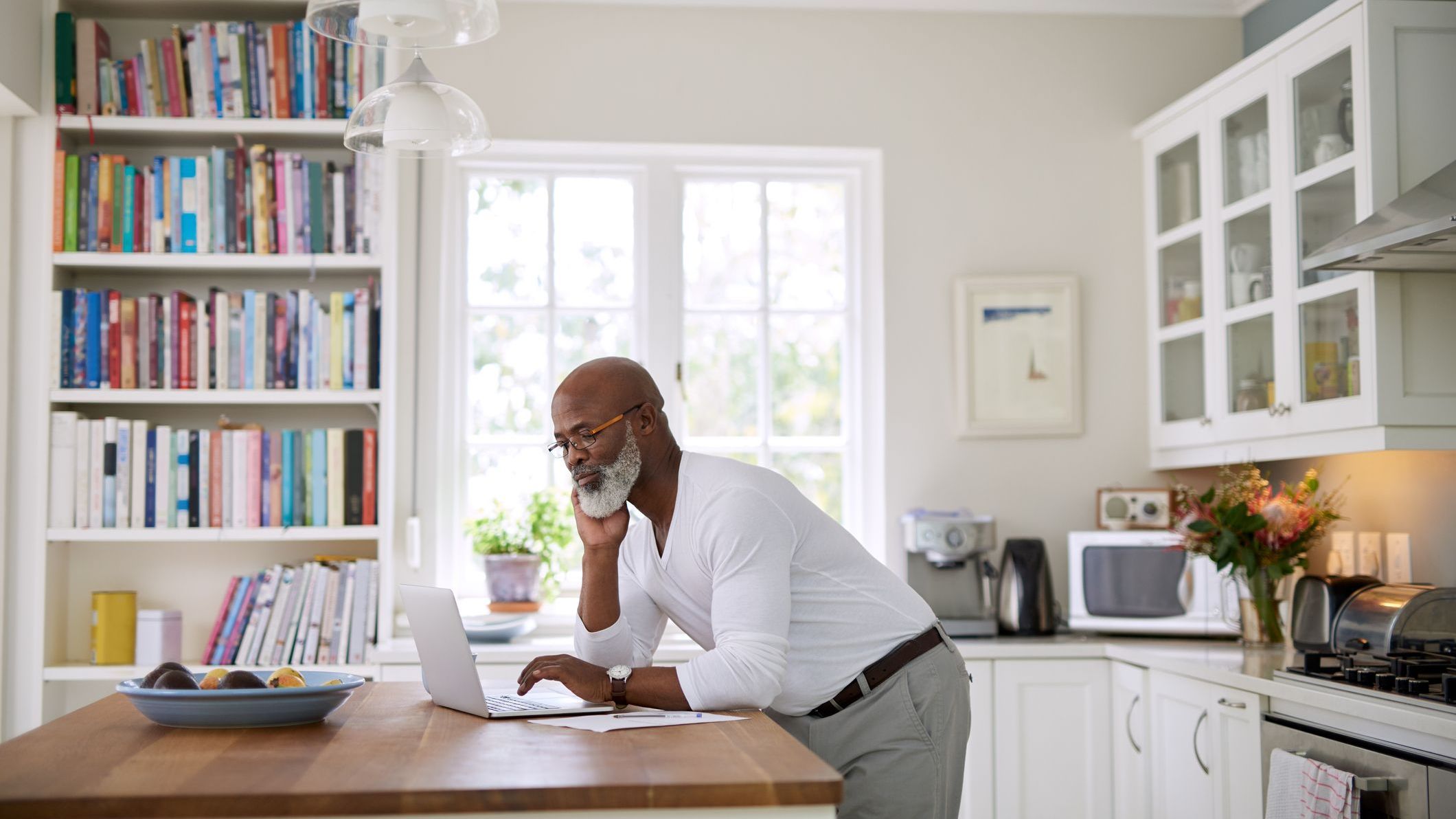 A man check his IRA balance on a laptop in his kitchen.