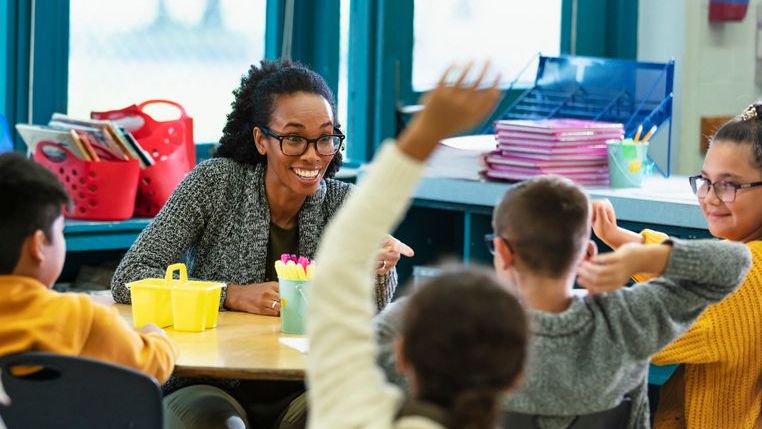 A teacher sits with students during a lesson.